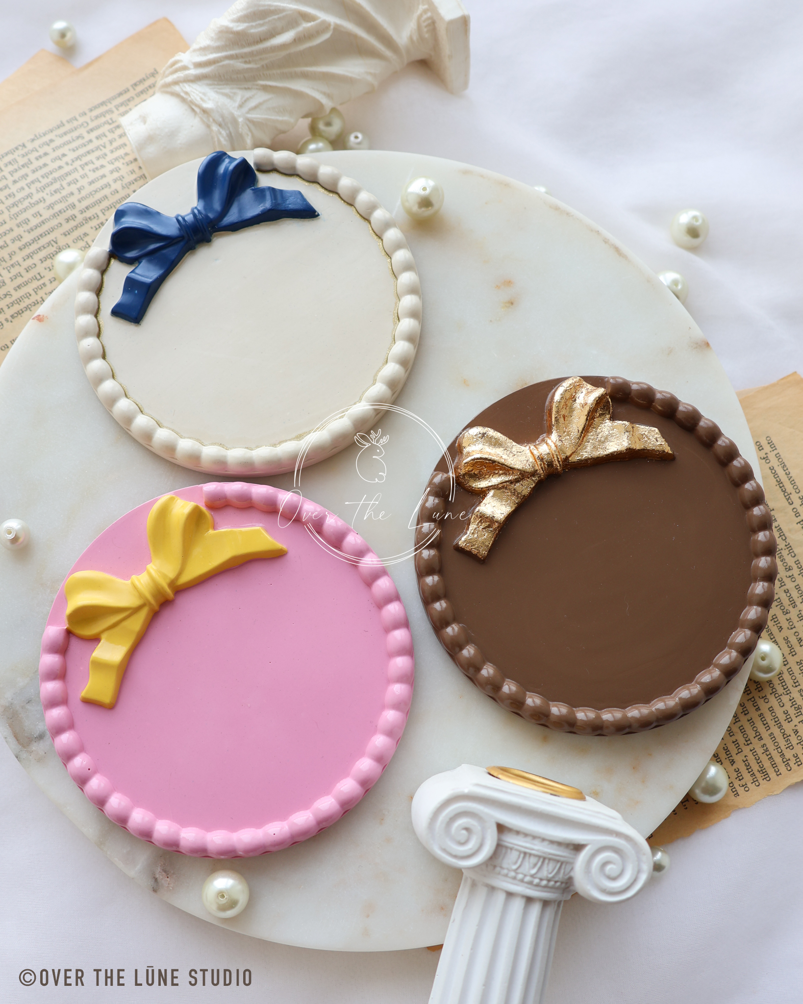 Three round decorative plaque or sign with a yellow bow design and a beaded border, displayed on a white marble surface.