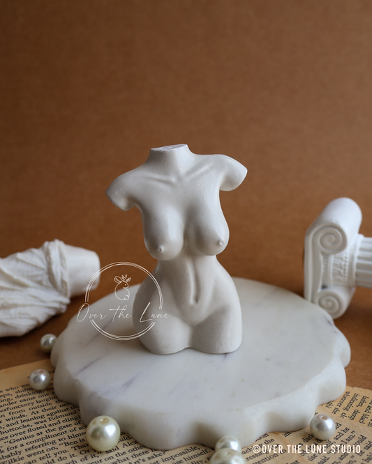 A white ceramic female torso bust display stand on a scalloped white marble base, styled with faux pearls and vintage newspaper on a brown background.
